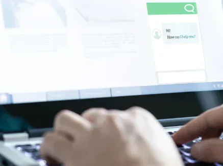 A person types on a laptop keyboard, with a chat window on the screen displaying the message, 