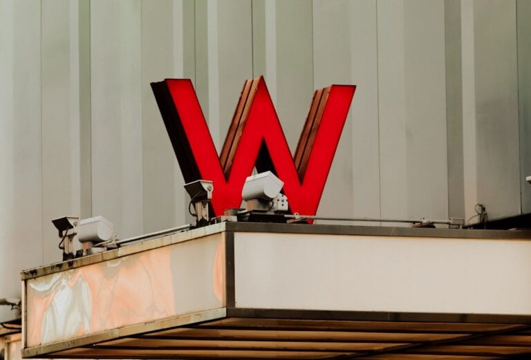 A large red letter "W" sign is mounted on the corner of a building facade with security cameras and a blank marquee below.