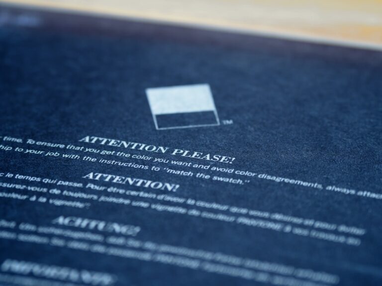 Close-up of a printed notice titled "ATTENTION PLEASE!" with a square color swatch above text giving instructions to match colors carefully.