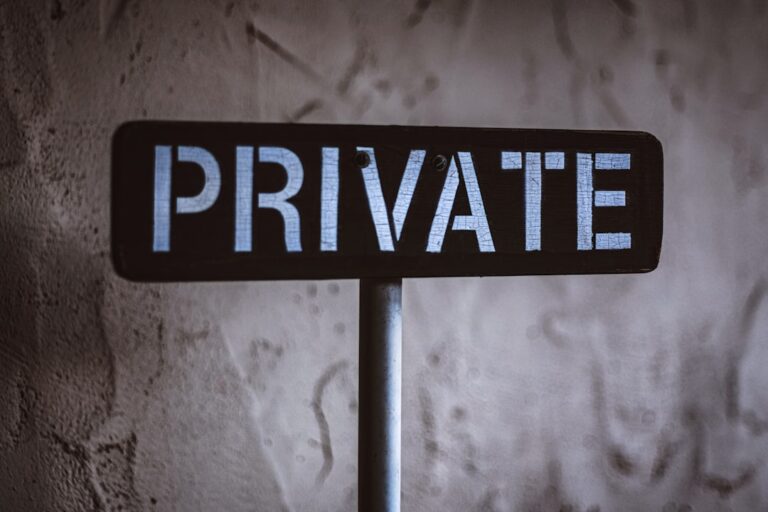 A black sign with the word "PRIVATE" in white capital letters, mounted on a metal post against a textured wall background.