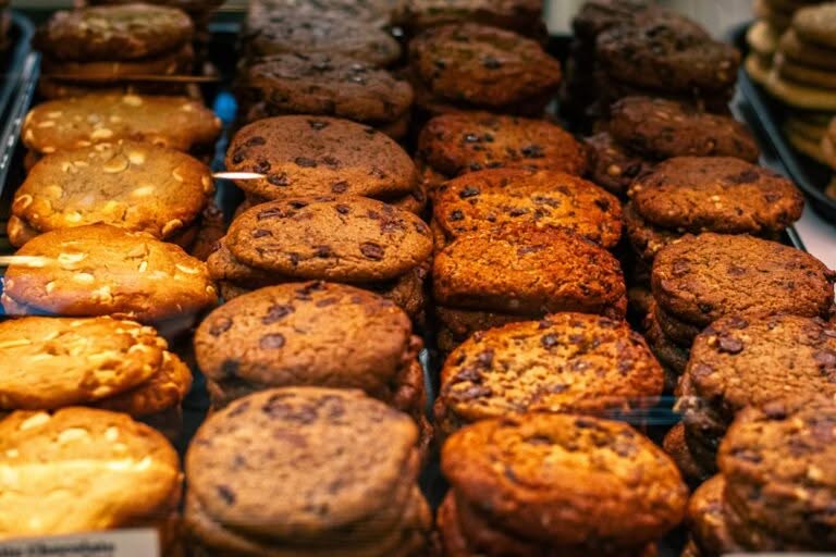 Rows of assorted cookies, including chocolate chip and nut varieties, displayed in a bakery case.